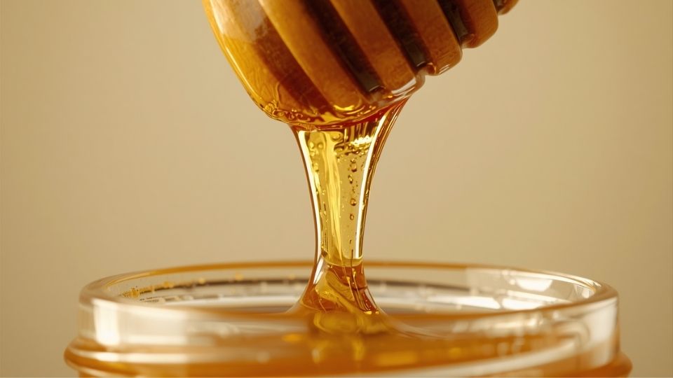 Close-up tetesan madu kental mengalir dari sendok kayu ke dalam botol, menunjukkan kekentalan dan warna keemasan madu asli