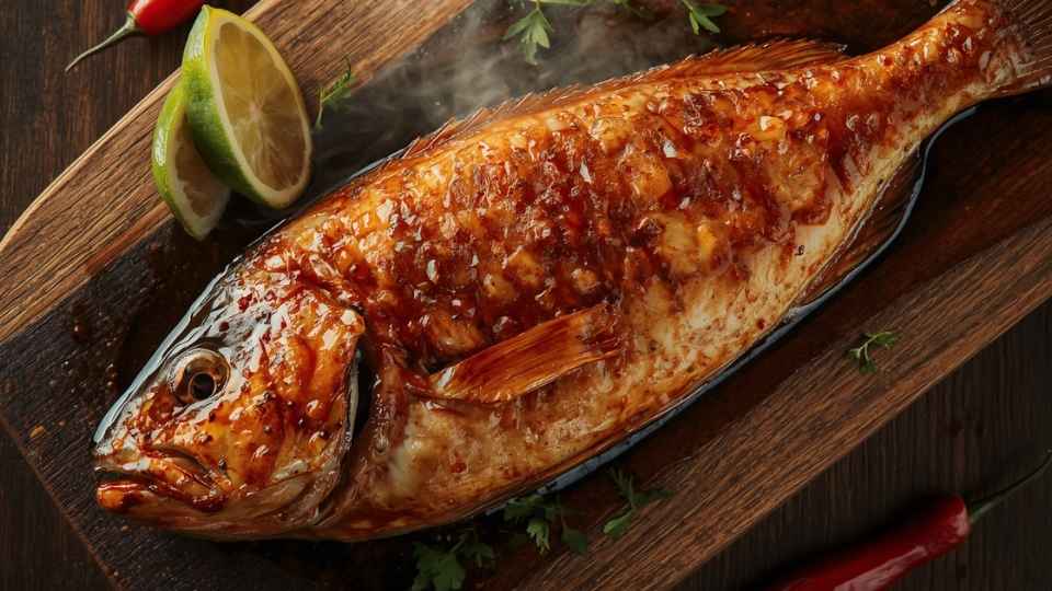 Ikan kakap bakar dengan olesan madu keemasan mengilap di atas talenan kayu, disajikan dengan irisan jeruk nipis dan cabai merah — resep ikan kakap bakar madu anti gosong