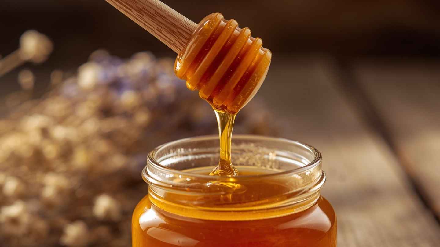 Madu asli menetes dari sendok kayu ke toples kaca, menunjukkan tekstur dan keaslian madu