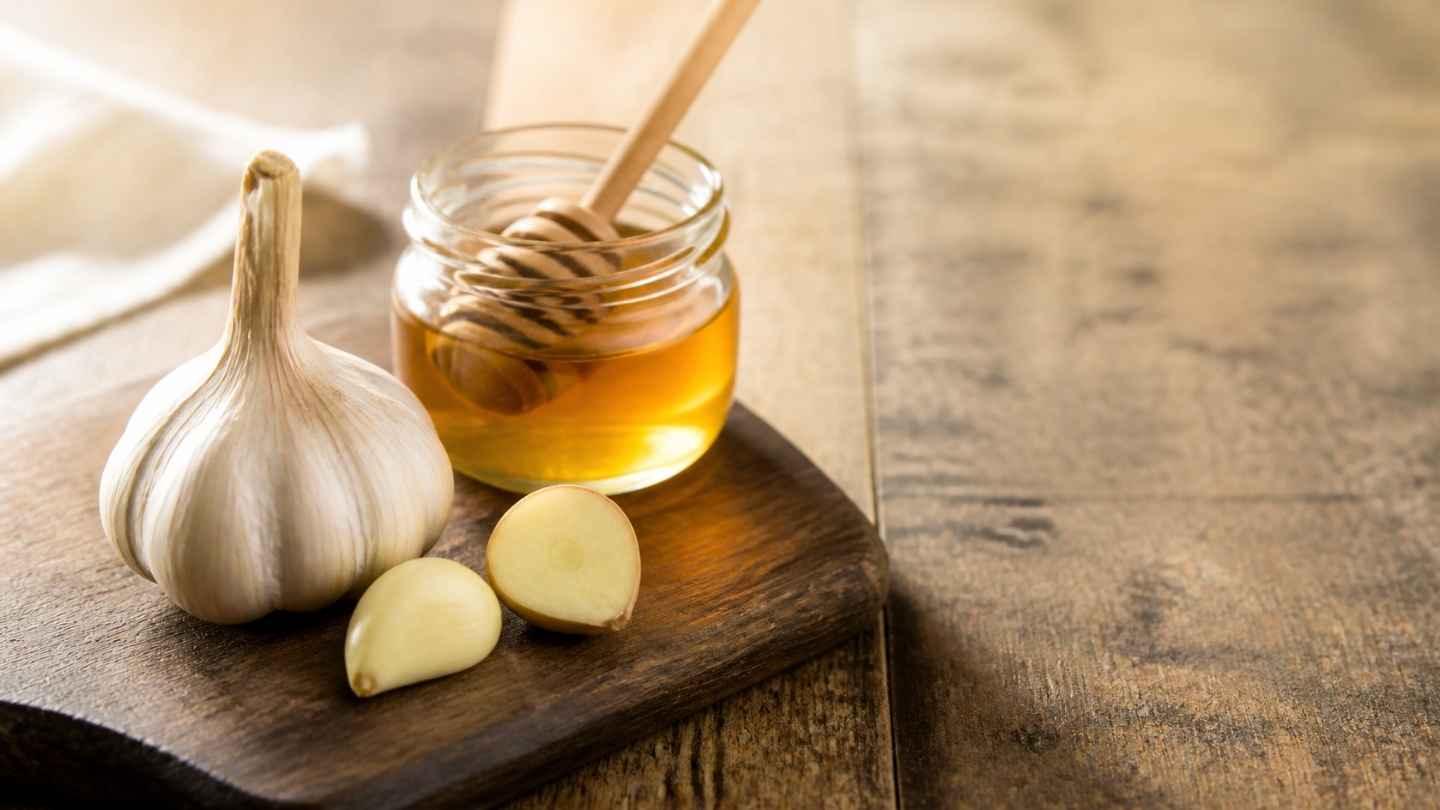 Bawang lanang utuh dan madu murni dalam jar kaca di atas kayu gelap sebagai ilustrasi manfaat bawang lanang dan madu untuk pria