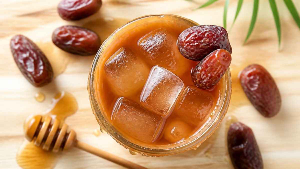 Segelas jus kurma madu kental dengan es batu dan taburan kurma di tepi gelas, resep jus kurma madu