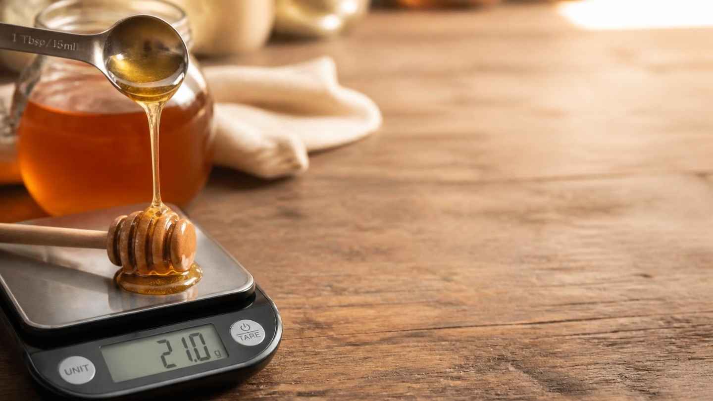Sendok makan berisi madu murni di atas timbangan digital, takaran 1 sdm madu sekitar 21 gram dan 64 kalori
